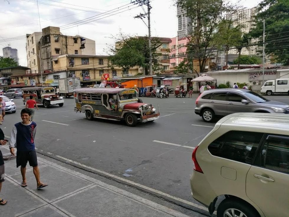 Bustling street with jeeps, cars, pedestrians, and buildings in an urban area.