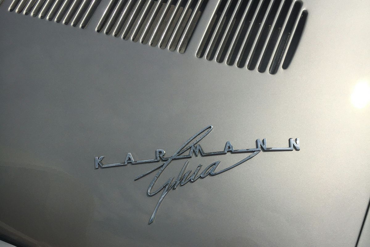 Close-up of a silver car hood with "Karmann Ghia" emblem.