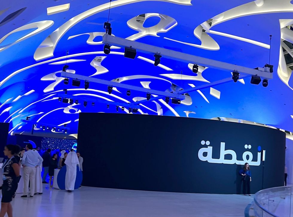 futuristic blue-lit interior with people, featuring Arabic script on a large display