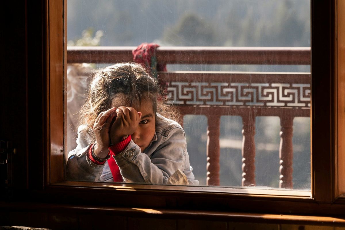 girl looking through a window with mountains and trees in the background