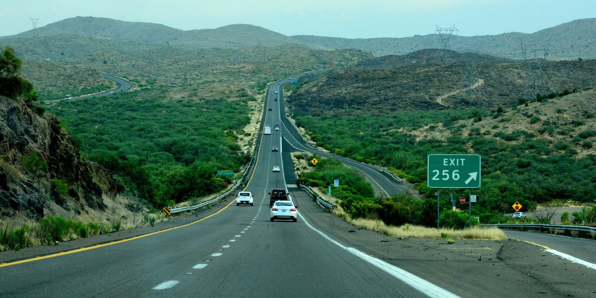 gray concrete road between green grass-covered mountains during daytime