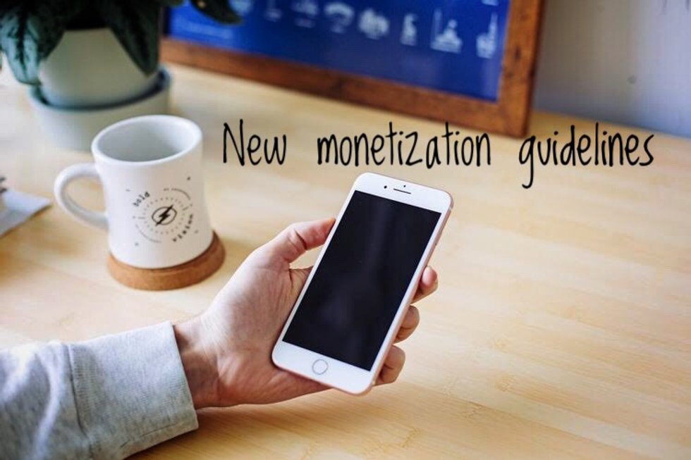Hand holding smartphone, coffee mug nearby, text reads "New monetization guidelines."