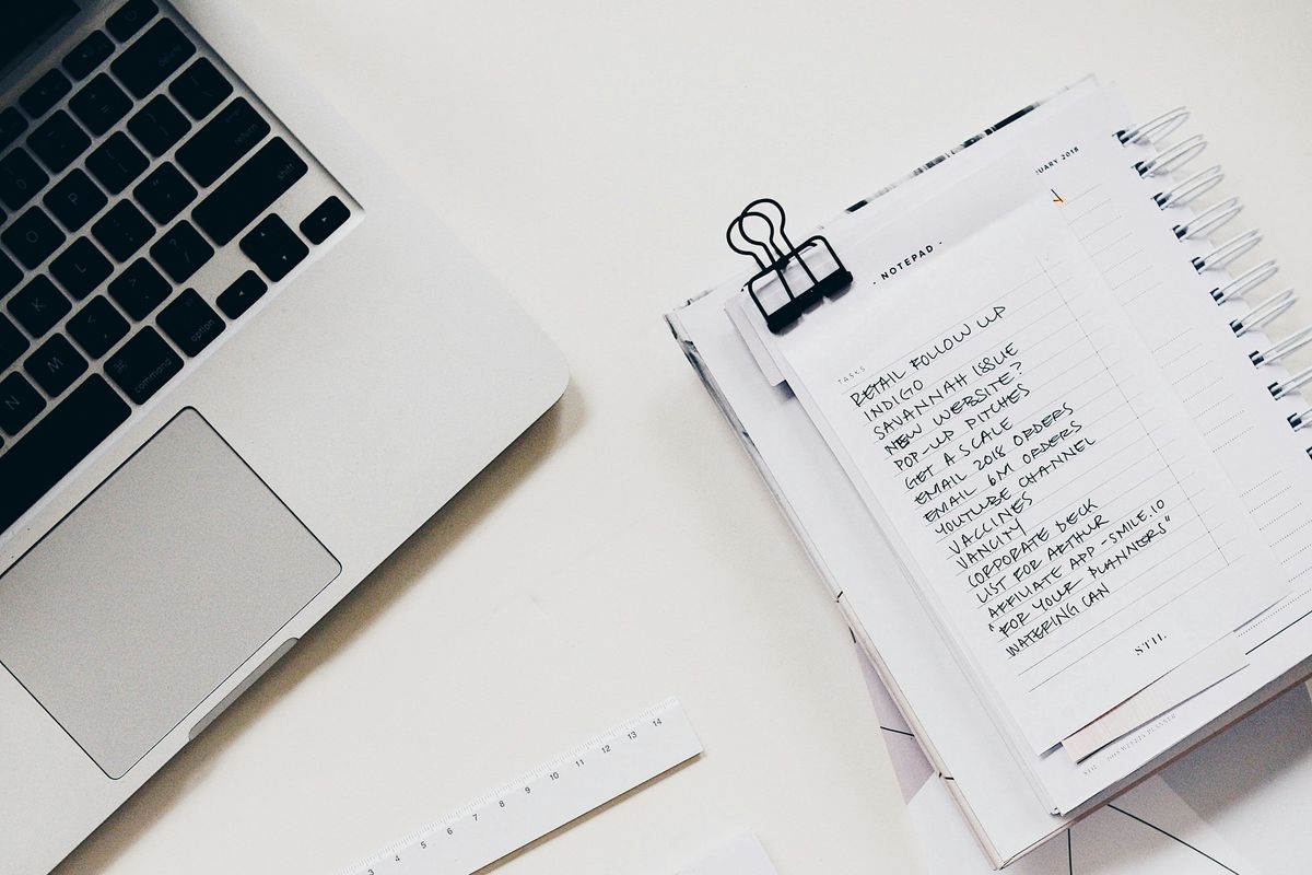 laptop and notepad on desk with handwritten task list