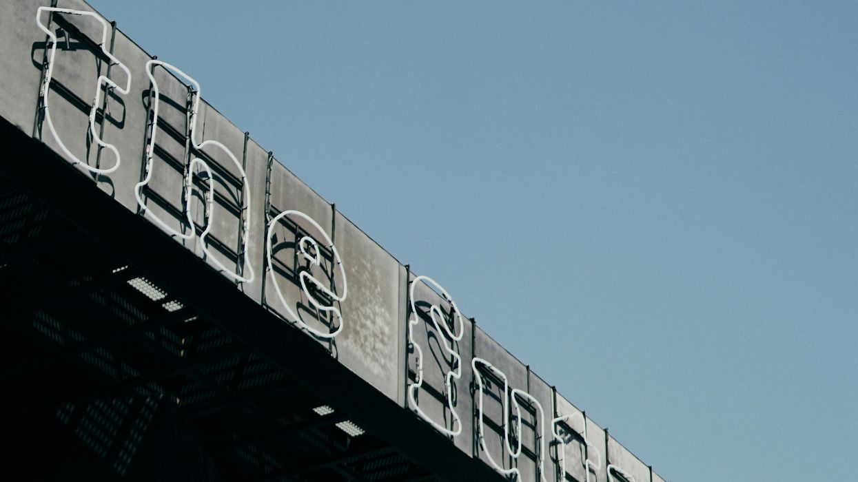 Neon sign on building edge against clear blue sky.