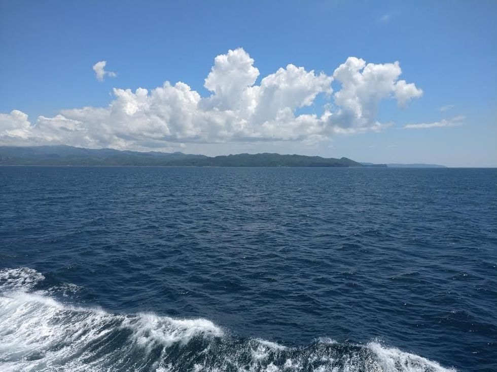 Ocean waves with distant mountains and fluffy clouds under a clear blue sky.