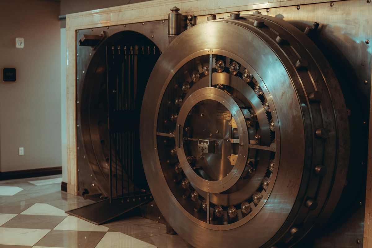 Open bank vault with a large, round metal door in a tiled room.