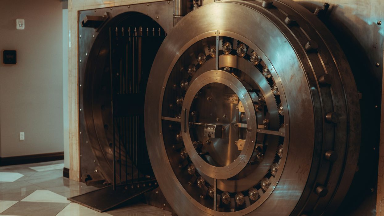 Open bank vault with a large, round metal door in a tiled room.