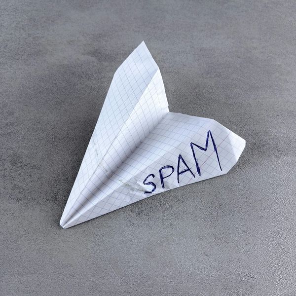 paper airplane with "SPAM" written on it, on a textured surface
