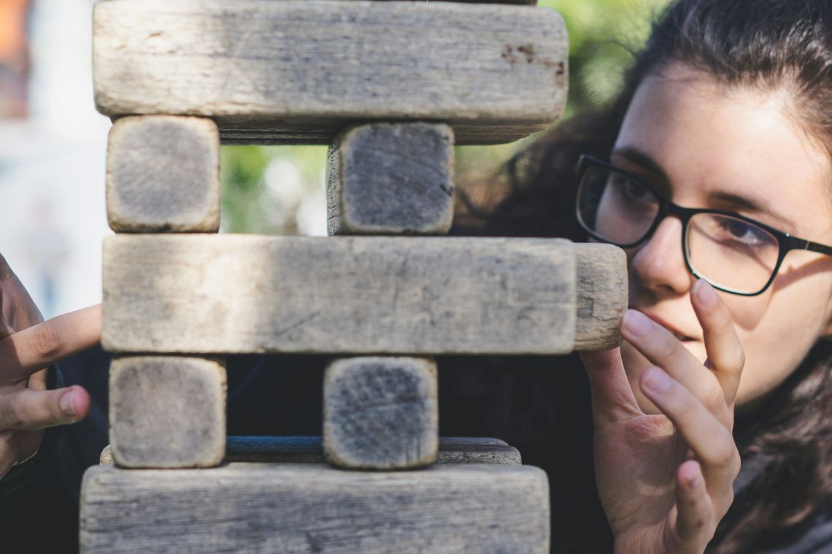 Person focusing on a large Jenga tower outdoors.