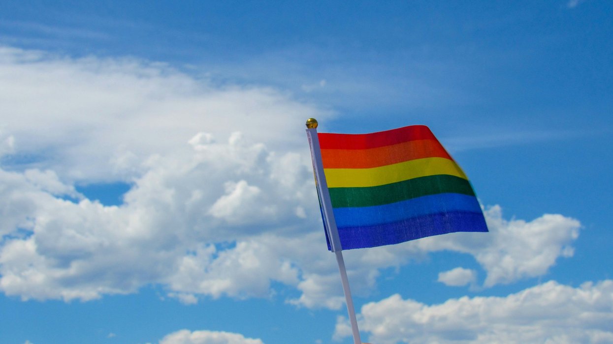 person holding flag of lgbtq under white clouds and blue sky during daytime