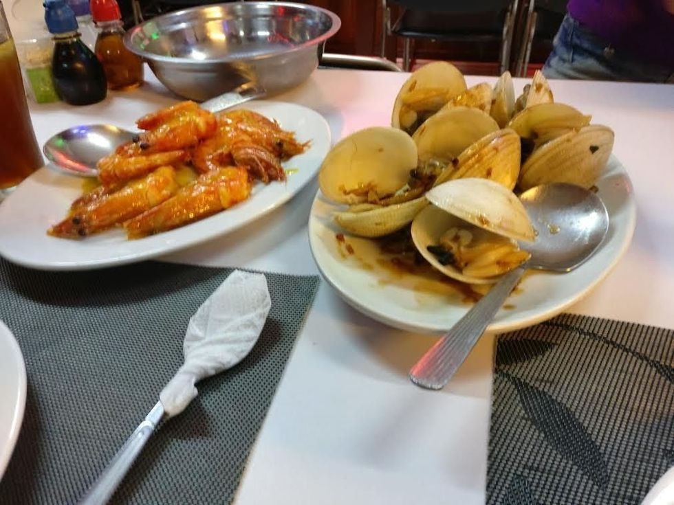 Plates of cooked shrimp and clams with sauce on a table setting.