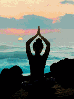 Silhouette of a person meditating by the ocean at sunset.