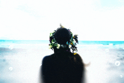 Silhouette with a flower crown facing a bright, blurry ocean scene.