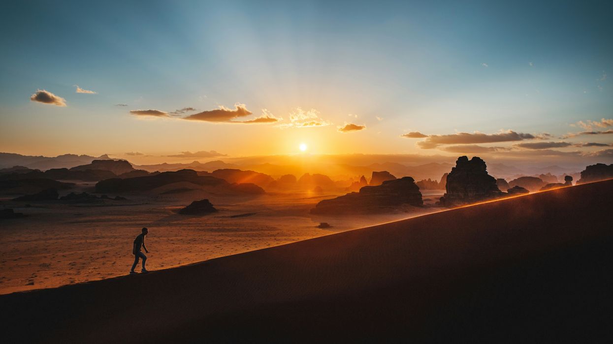 Silhouetted person climbing sand dune at sunset with scenic desert landscape.