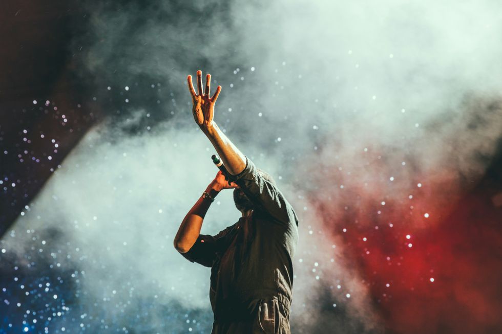 singer on stage with microphone, hand raised, against a smoky, starry backdrop
