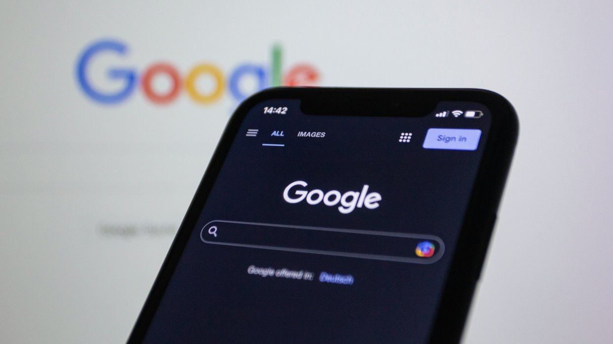 Smartphone displaying Google's dark theme search page, Google logo blurred in the background.
