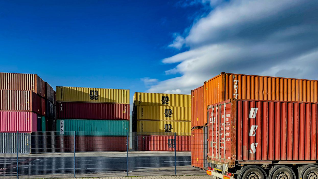 Stacked shipping containers and truck trailer under a blue sky with clouds.