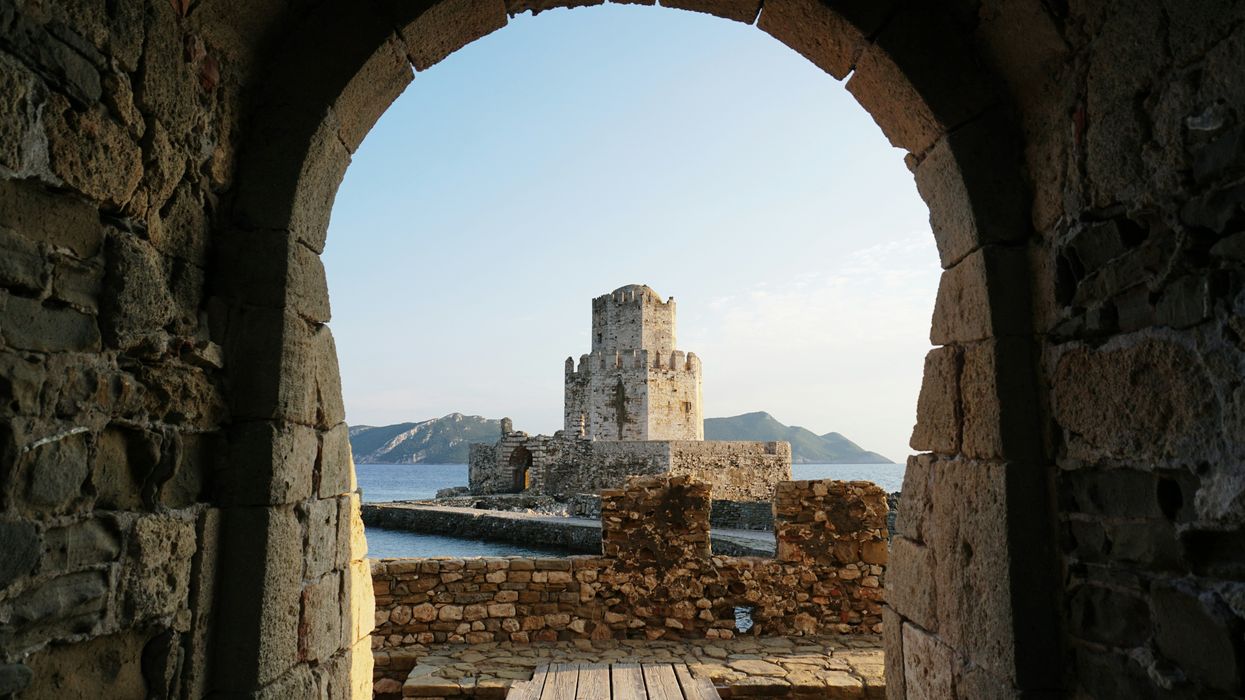 stone castle viewed through an arched gateway, with sea and hills in the background