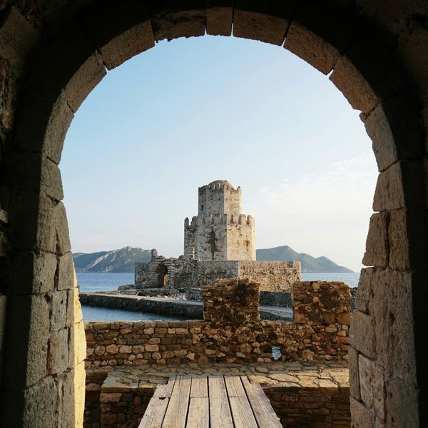 stone castle viewed through an arched gateway, with sea and hills in the background