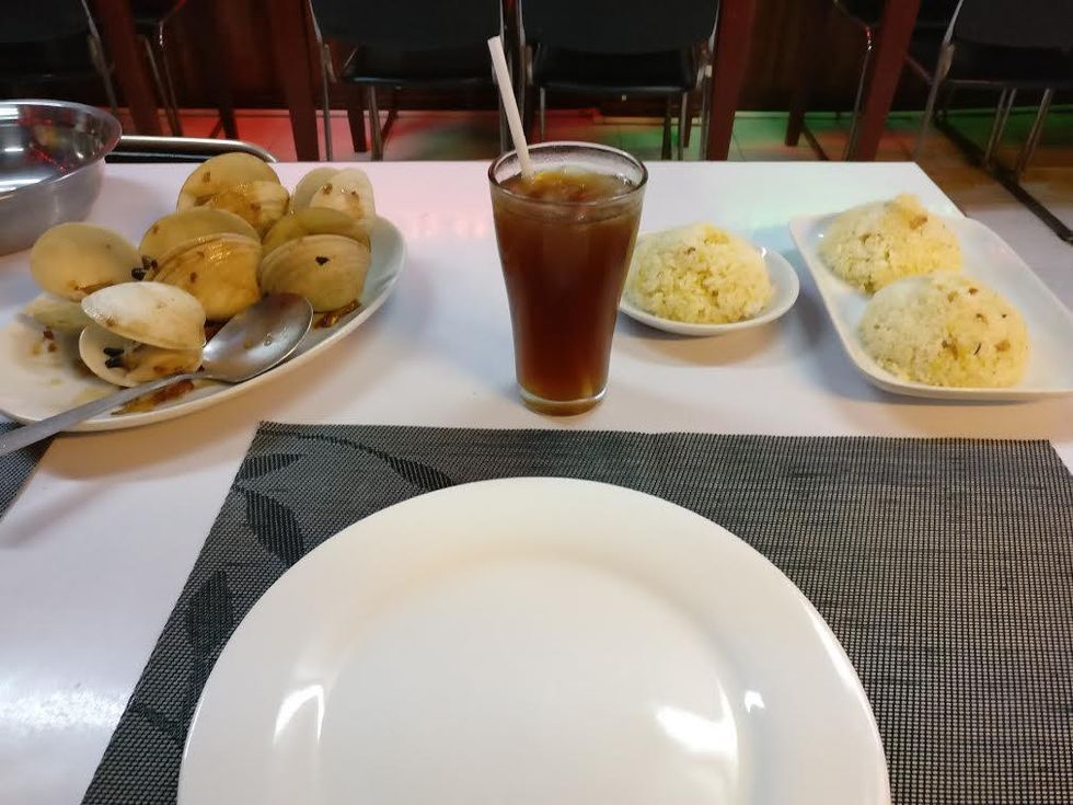 Table setting with dumplings, fried rice, iced tea, and an empty plate.