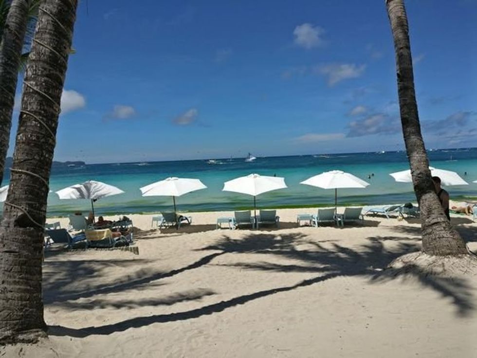 Tropical beach scene with white umbrellas, clear blue water, and palm trees.