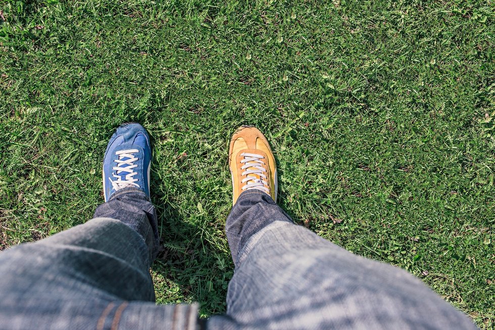 Two different colored sneakers on grass; blue on left, orange on right.