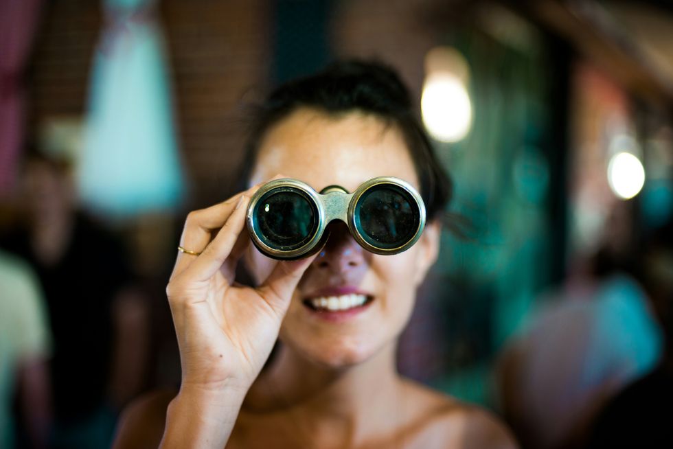 Woman smiling and looking through binoculars indoors.